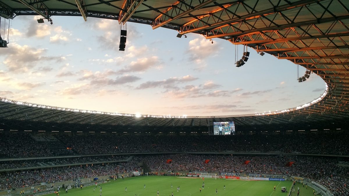 Packed football stadium during a match at sunset with open roof
